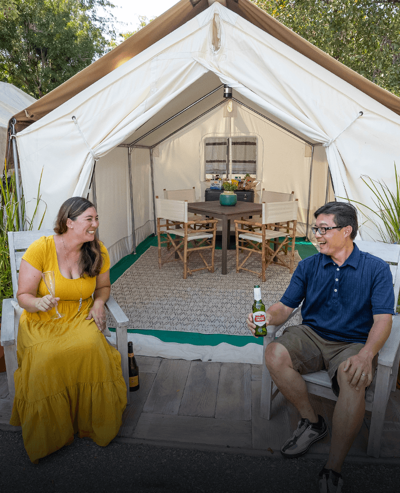 A couple sits at the entrance to a tent holding drinks
