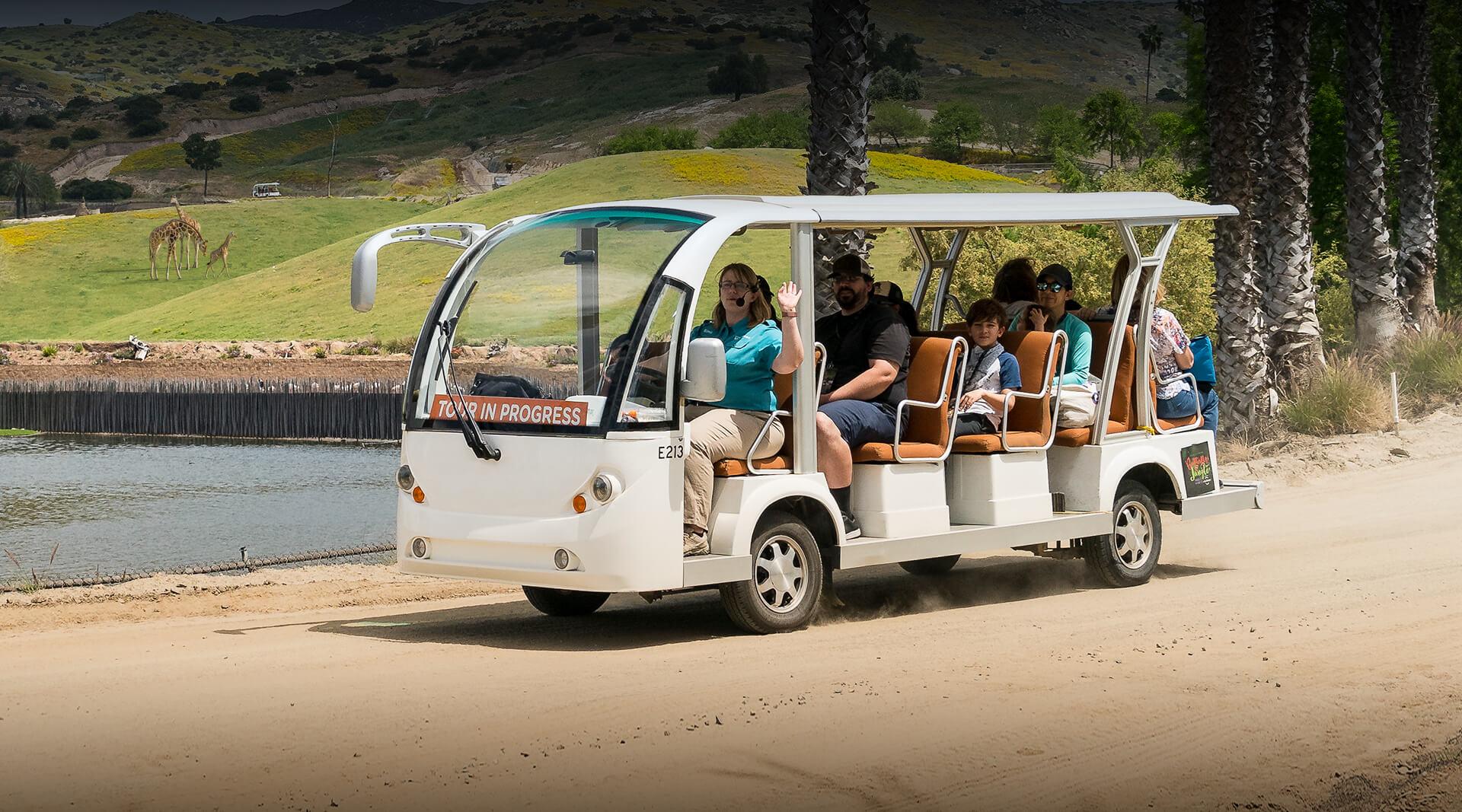 Safari cart transporting visitors along dirt road in front of large pond and field.